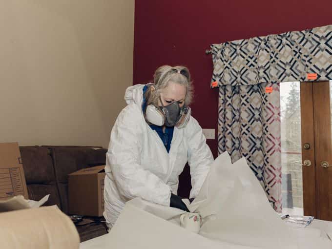 A technician in protective gear carefully wrapping contents inside a smoke-damaged home