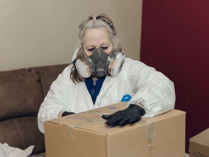 A technician in a respirator and protective suit sealing a packed box